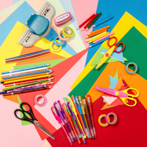 Craft supplies like scissors and colored pencils arranged over different colors of paper