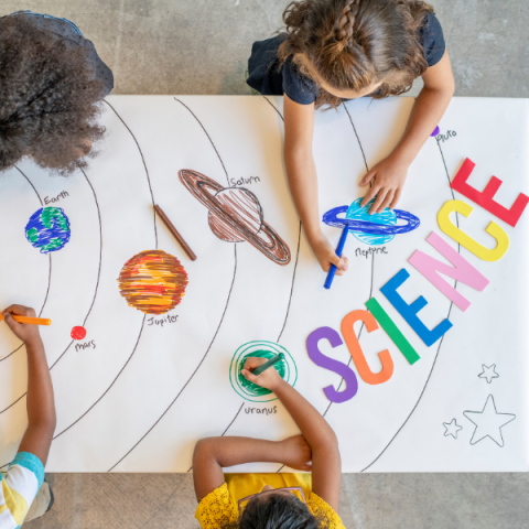 Overhead perspective of children coloring large "Science" banner