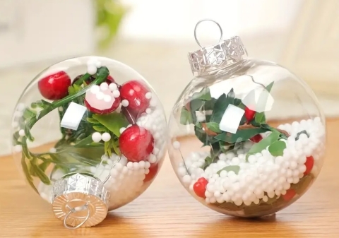 2 transparent ornaments filled with artificial snow and green sprigs with red berries 