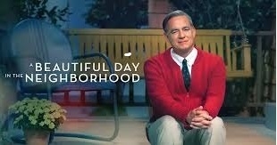 Tom Hanks playing Mr. Rodgers sits on his porch steps with a porch swing in the background