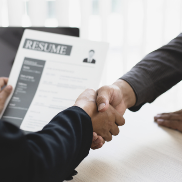 Two people shaking hands while one holds a resume