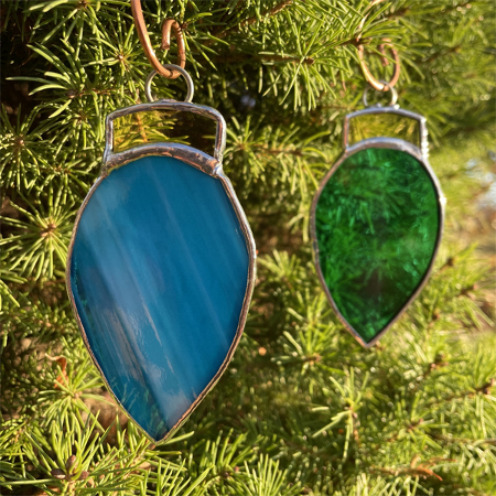 Colorful glass suncatchers shaped like holiday light bulbs, hanging from an evergreen tree.